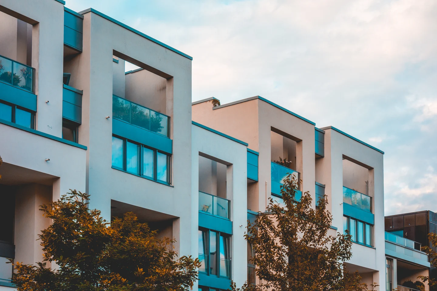 Moderne Mehrfamilienhäuser mit hellen Fassaden, Glasbalkonen und Bäumen – Symbolbild zur Hausverwaltung
