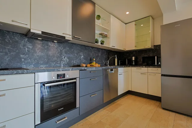 Offene Küche mit grauen und weißen Fronten, Backofen und Kühlschrank.